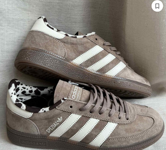 Pair of brown Adidas sneakers with white stripes on a gray background